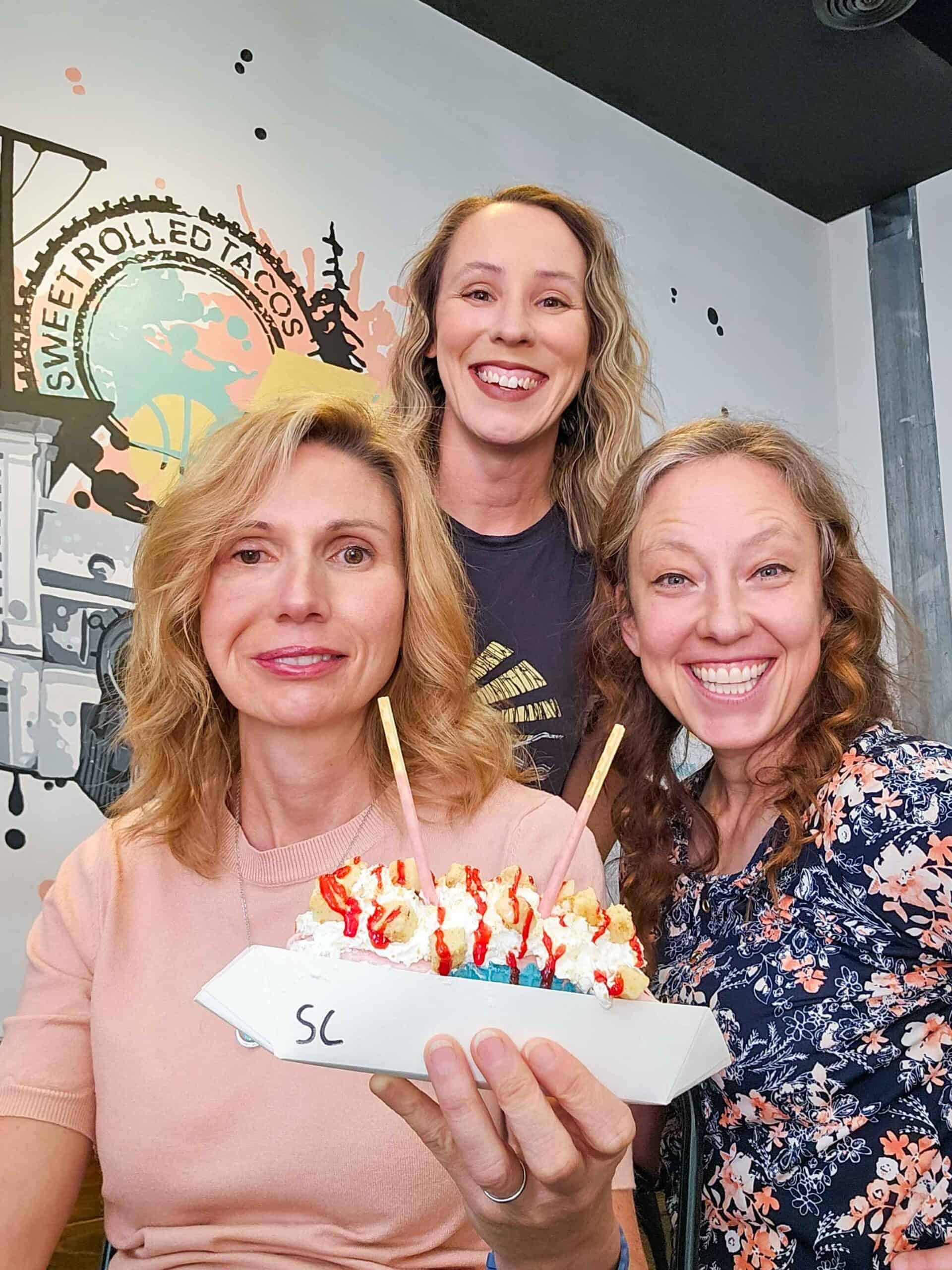 3 women smiling, one holding an ice cream taco