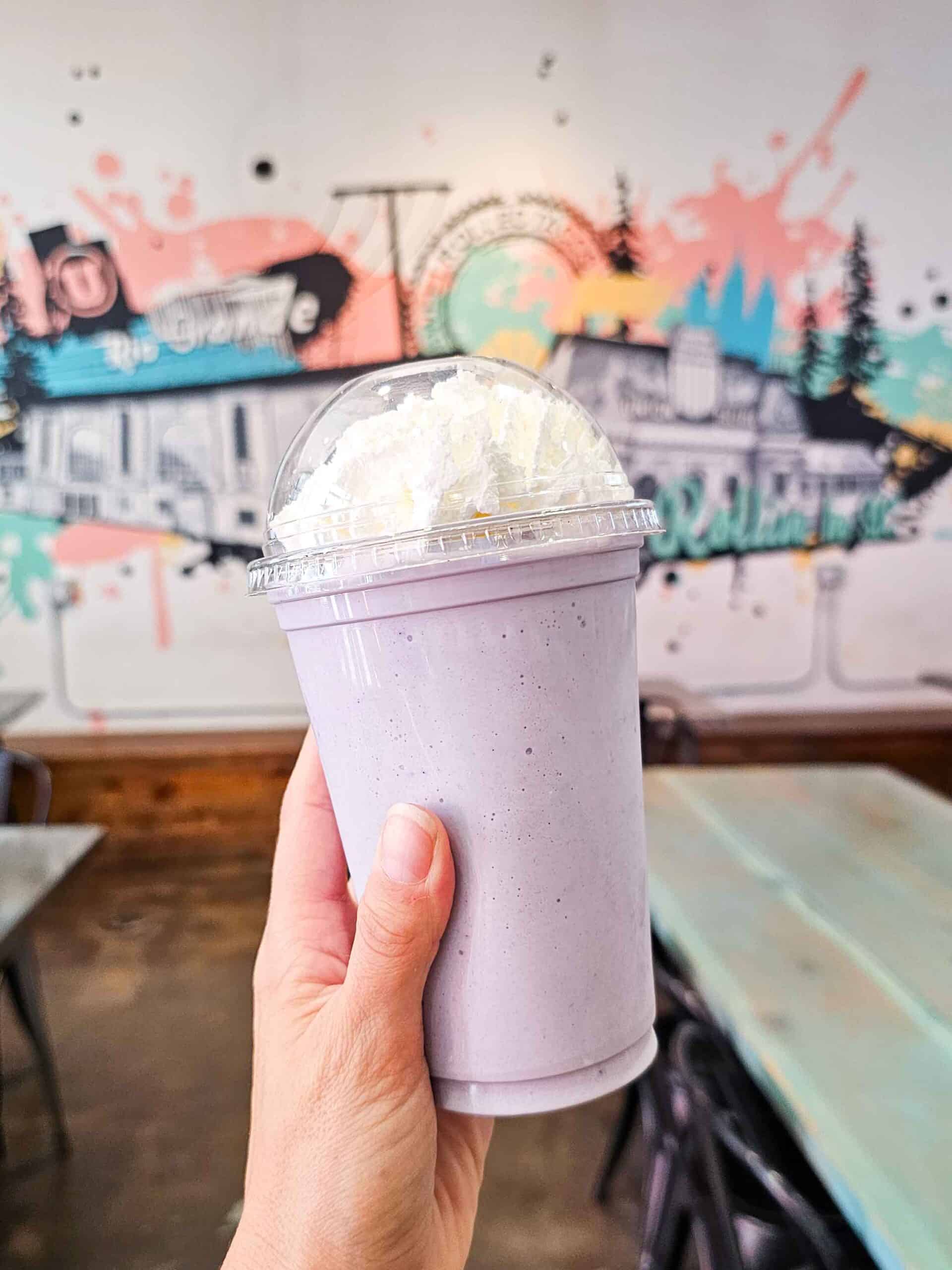 hand holding a purple milkshake with whipped cream