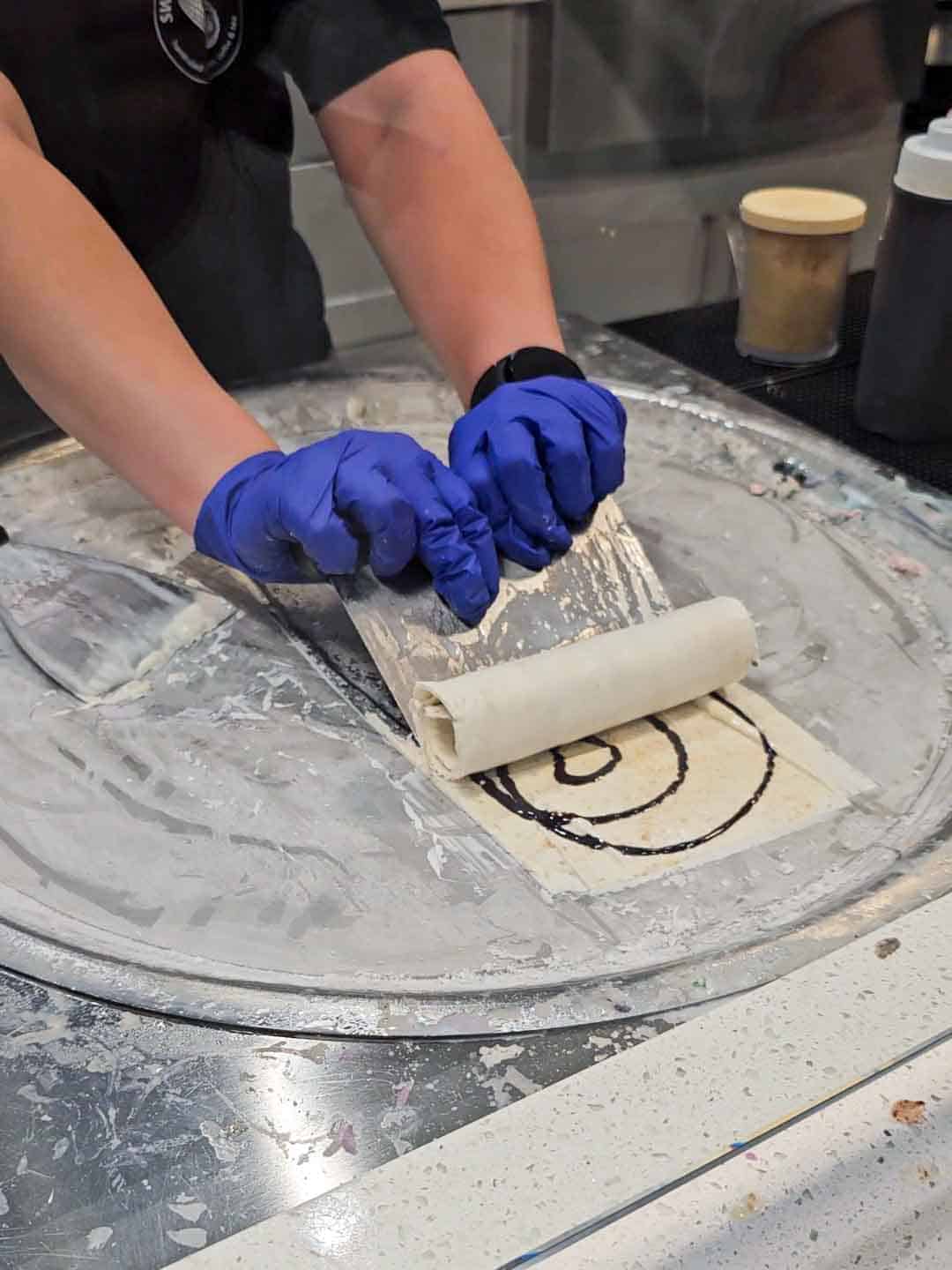 hands using a scraper to roll a thin layer of ice cream