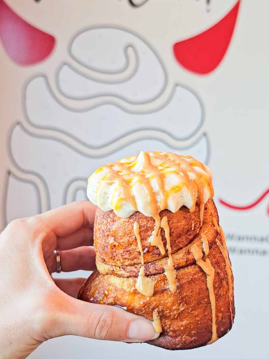 a tall cinnamon roll with frosting and peanut butter drizzle