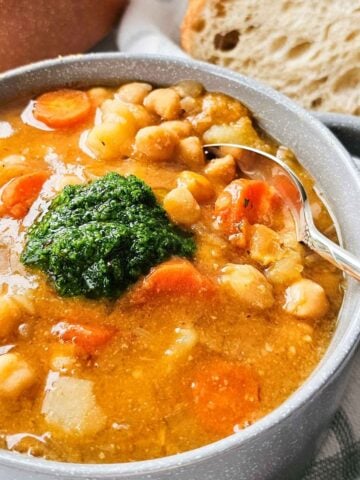 bowl of soup with chickpeas, potatoes, and carrots with a dollop of pesto